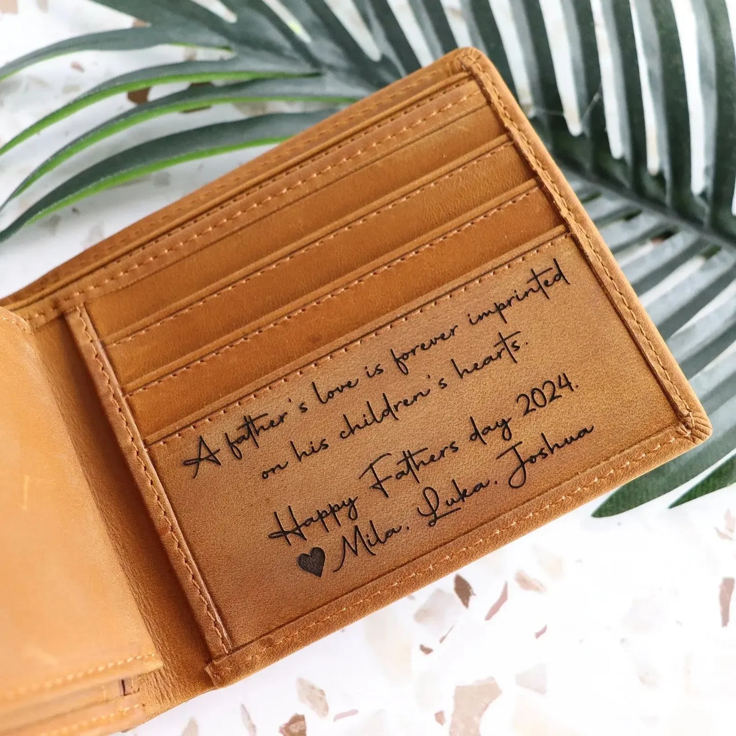 Engraved tan leather wallet with Father's Day 2024 message, on tropical leaf background