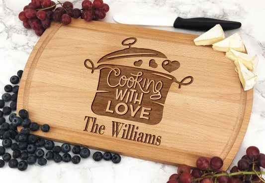 Custom engraved wooden cutting board with 'Cooking With Love' text, grapes, blueberries, cheese knife on marble surface