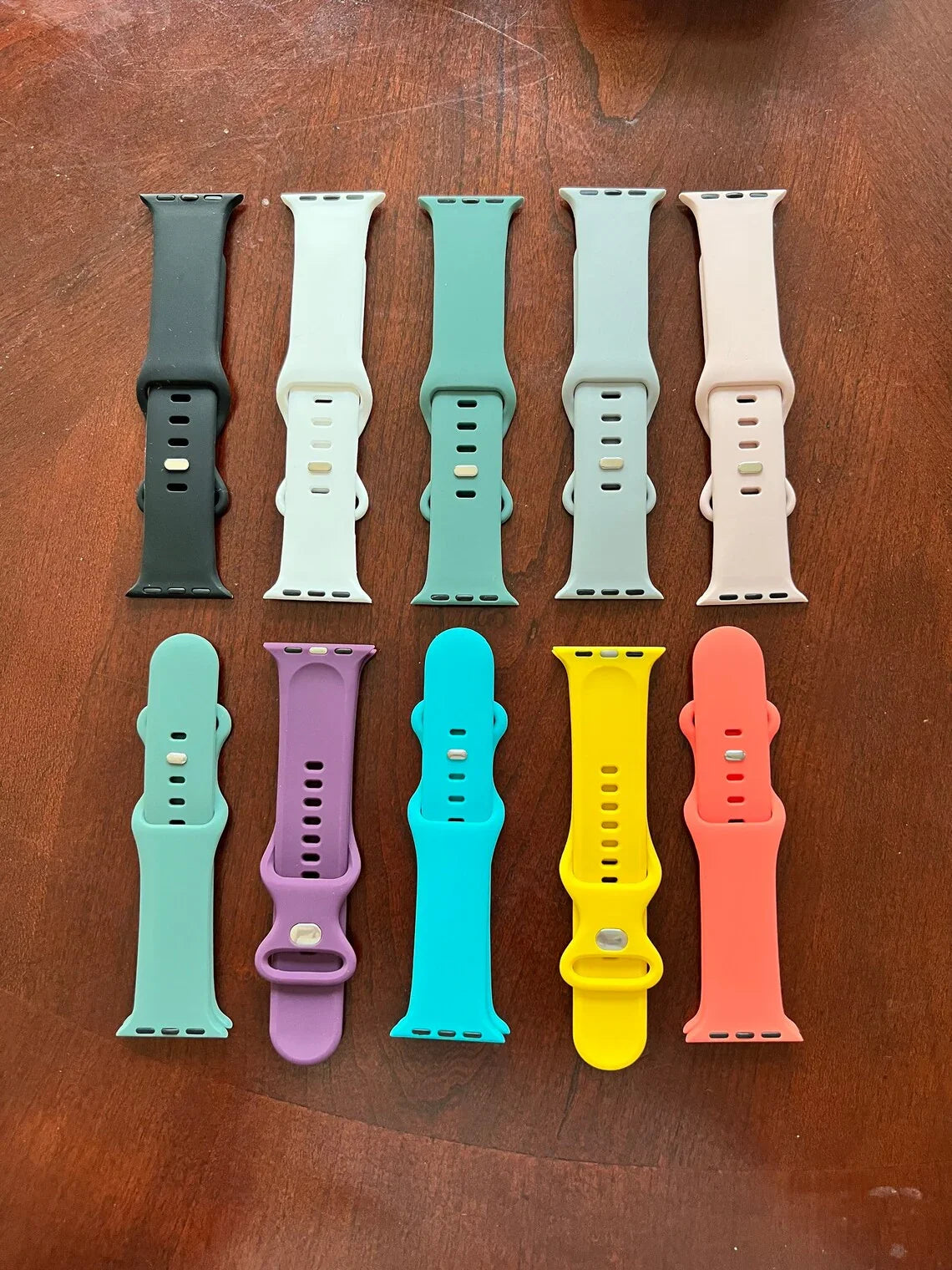 Colorful silicone Apple Watch straps in ten different colors on a wooden surface