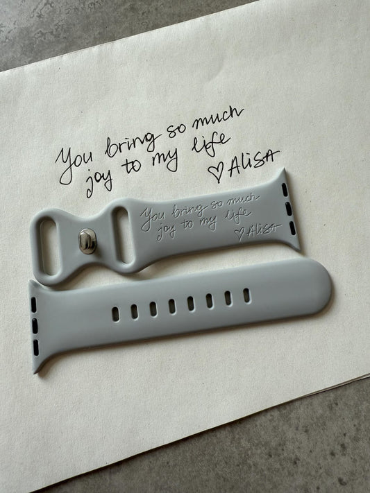Personalized grey Apple Watch strap on paper with handwritten 'You bring so much joy to my life.'
