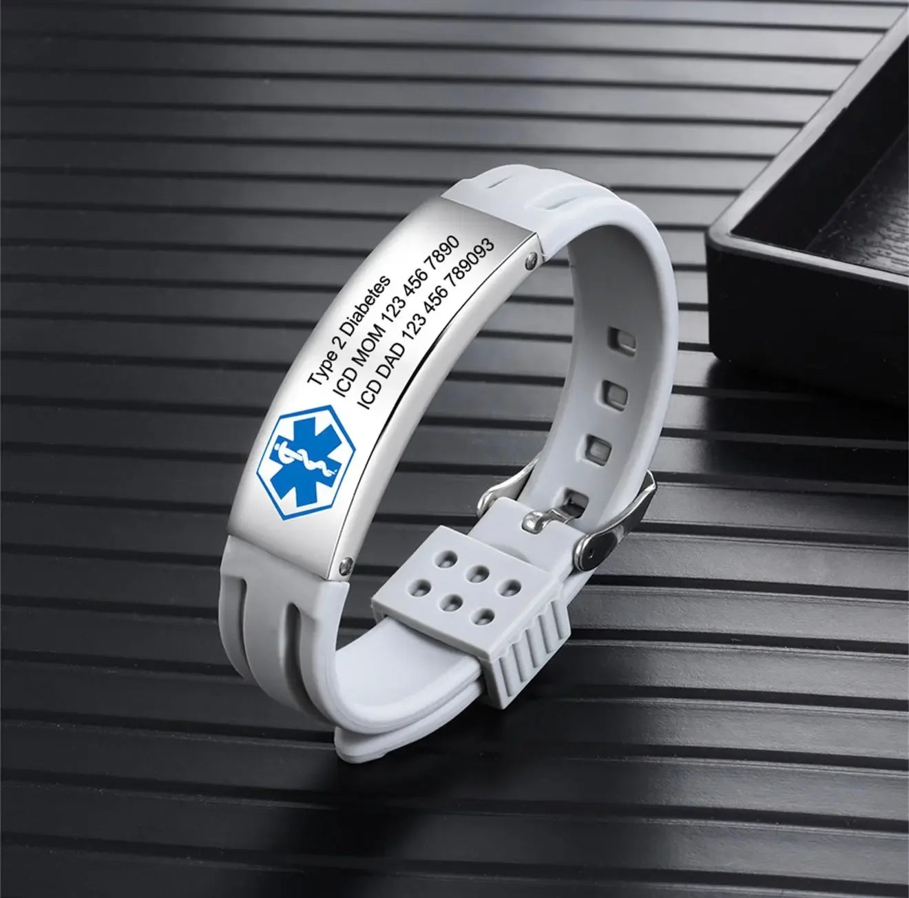 White medical alert ID bracelet for diabetes with engraved emergency contact information on black surface.