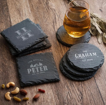 Personalized black slate coasters with engraved names on wooden table, glass of whiskey on coaster.