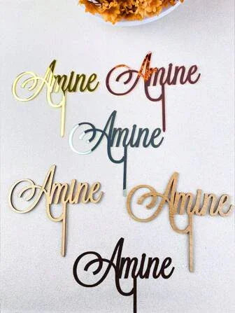 Custom cake toppers spelling Amine in various metallic and wooden finishes on a light background