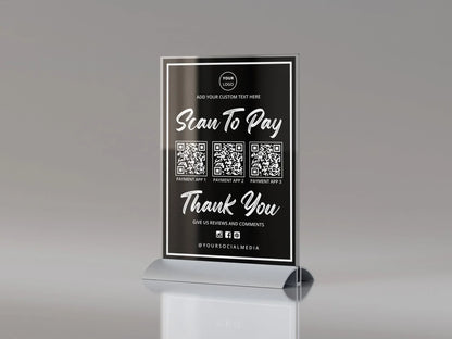 Black acrylic table sign with scan to pay QR codes and social media icons on a gray background.