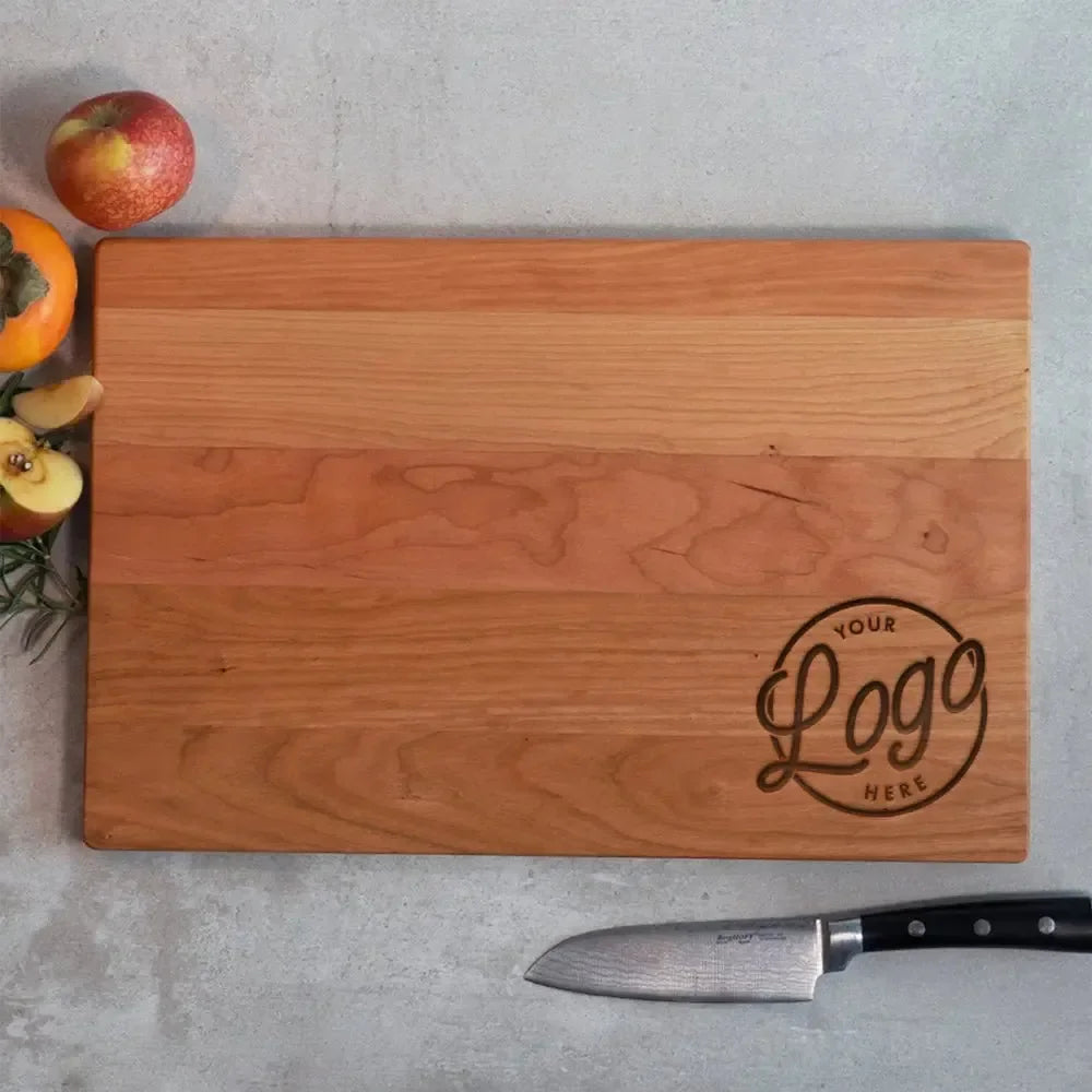 Custom wood cutting board with engraved logo, chef knife, and fresh fruit on countertop
