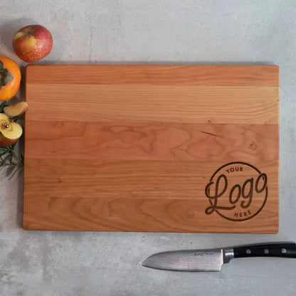 Custom wood cutting board with engraved logo, chef knife, and fresh fruit on countertop