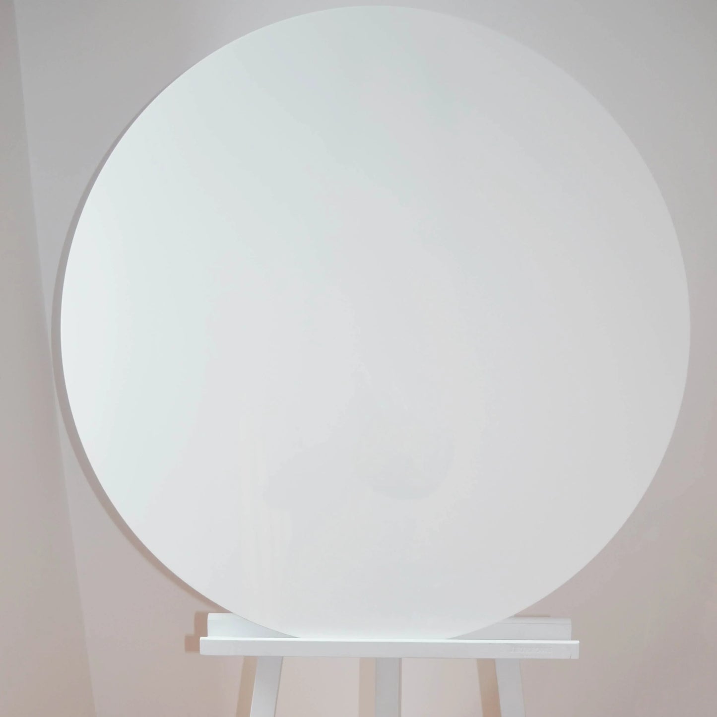 Large white round acrylic display board on easel against light wall