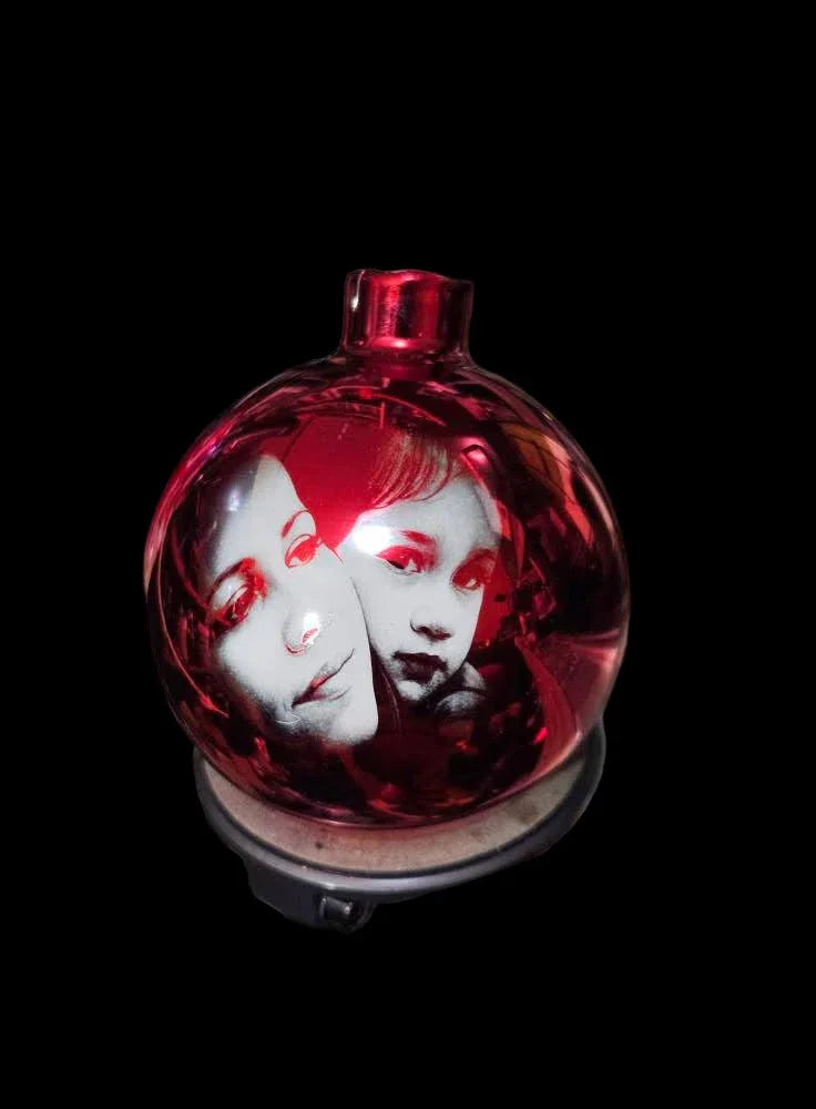 Red glass orb with etched portraits of two faces on a black background