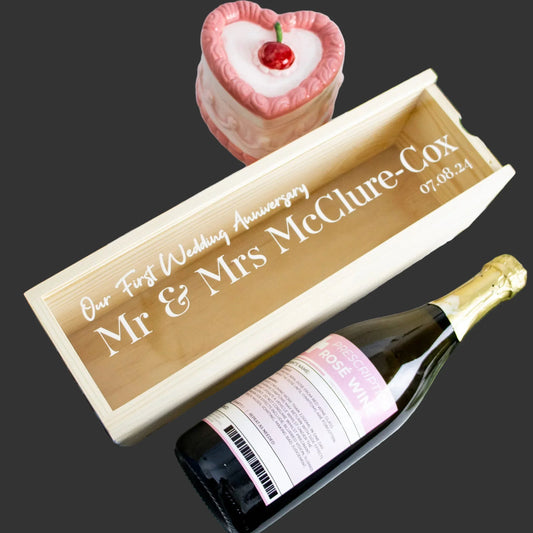 Printed wooden wine and champagne box with engraved wedding anniversary text, a wine bottle, and a pink heart-shaped cake on a dark background.
