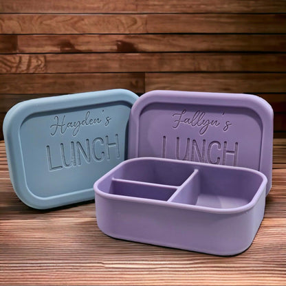 Two lunch containers with personalised names on a wooden surface