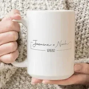 Personalised couples coffee mug with custom names and date, held by hands in a sweater